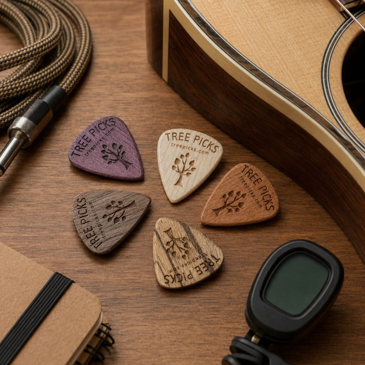 Wooden guitar picks with 'Tree Picks' branding on a wooden surface with a guitar and cable.
