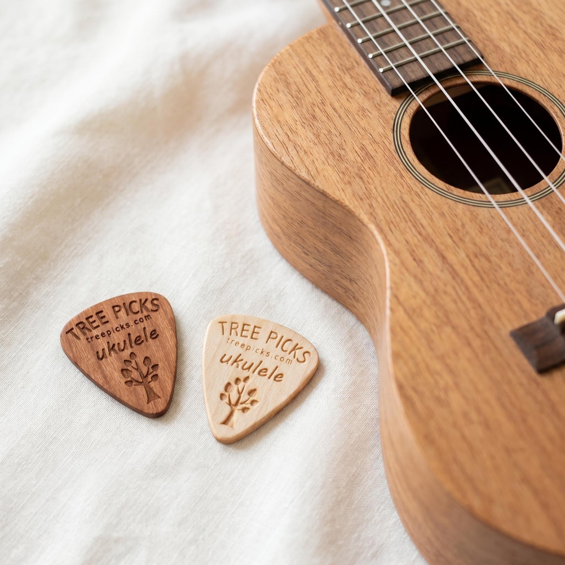 Two wooden ukulele picks with 'Tree Picks' branding next to a ukulele on a white background.