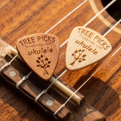 Two wooden ukulele picks on a ukulele strings with 'Tree Picks' branding.