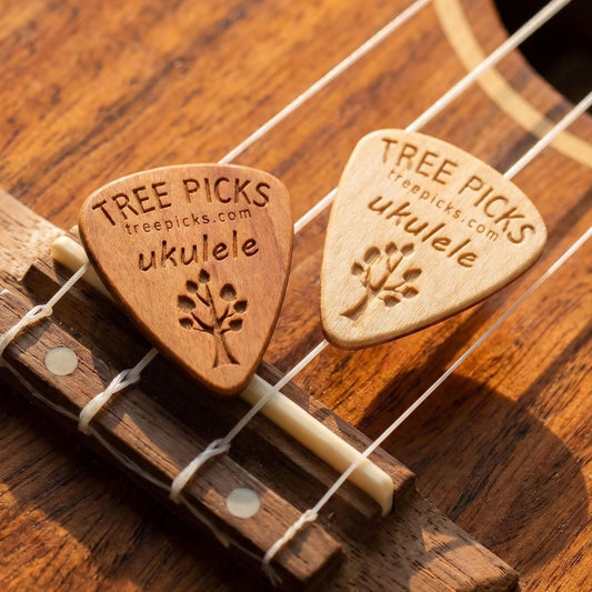 Two wooden ukulele picks on a ukulele strings with 'Tree Picks' branding.
