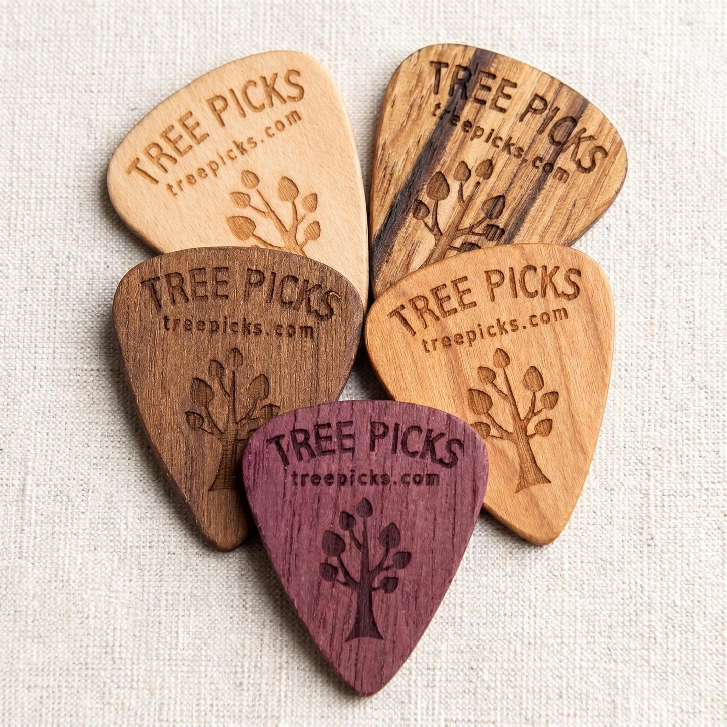 Set of wooden guitar picks with 'Tree Picks' branding on a textured fabric background